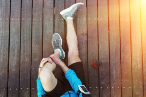 sportsman's legs sitting on the wooden floor with red sport plastic bottle, view from the top
