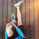 sportsman's legs sitting on the wooden floor with red sport plastic bottle, view from the top