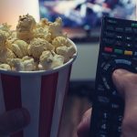 Pov shot from a young man watching a movie on a smarthome tv at home with popcorn box and TV Remote control in his hands. ideal for websites and magazines layouts