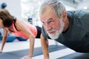 Senior couple in gym working out, doing push ups